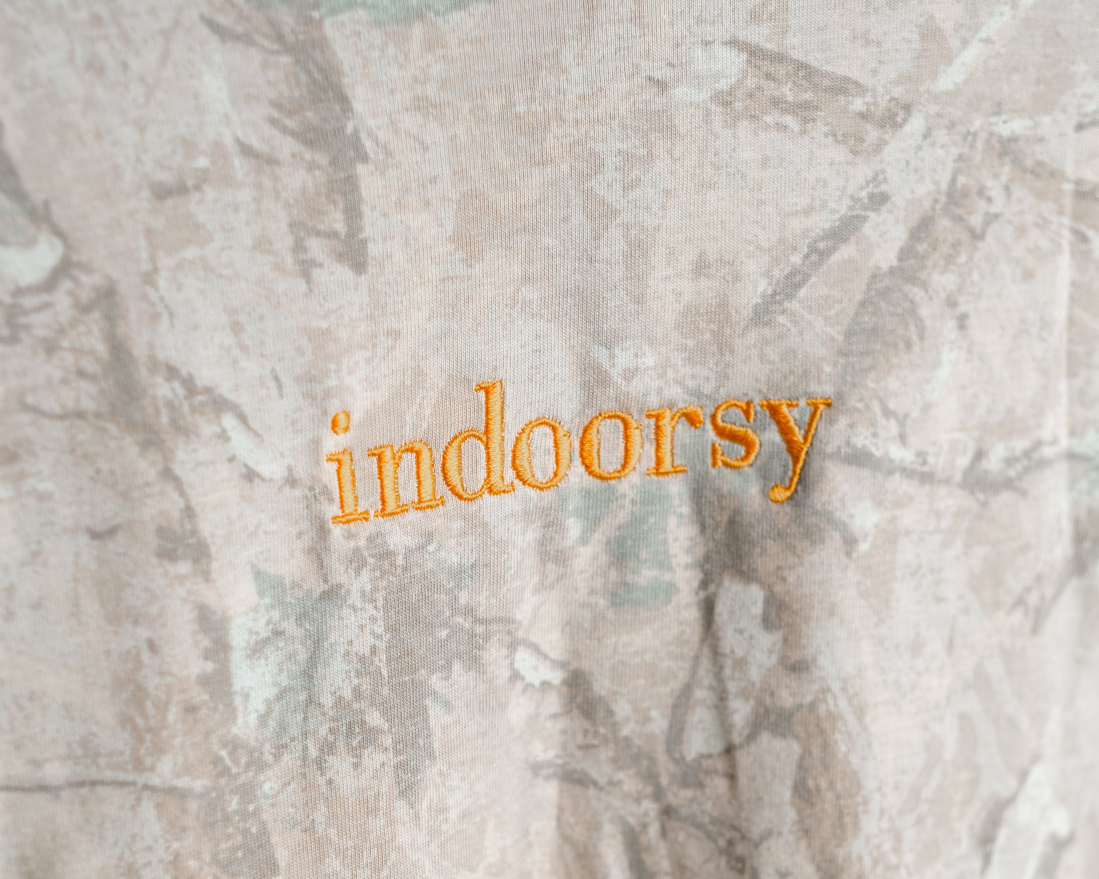 Camouflage-patterned fabric with 'indoorsy' text embroidered in orange.